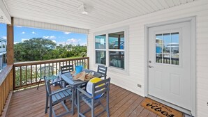 A covered outdoor area with a wooden deck, a table with chairs, and a door with windows.