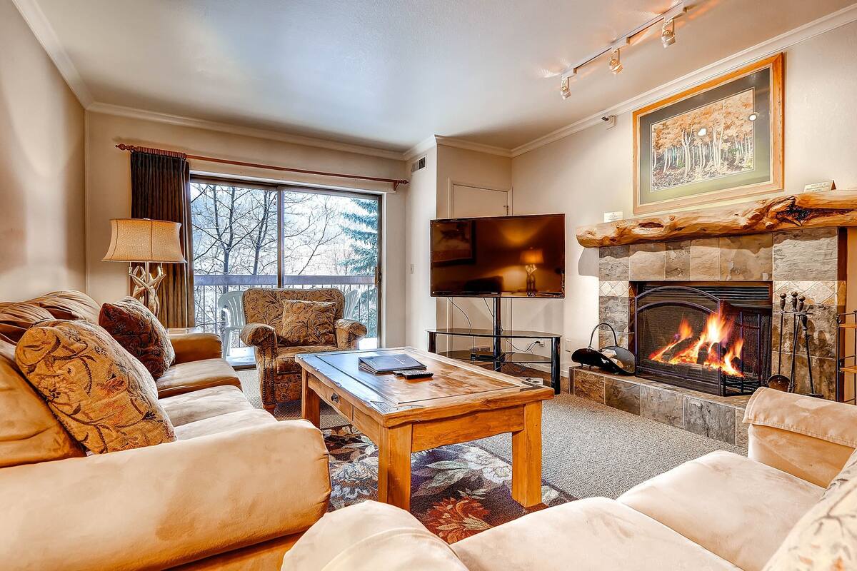 A cozy living room with a fireplace, comfortable seating, and a large window.