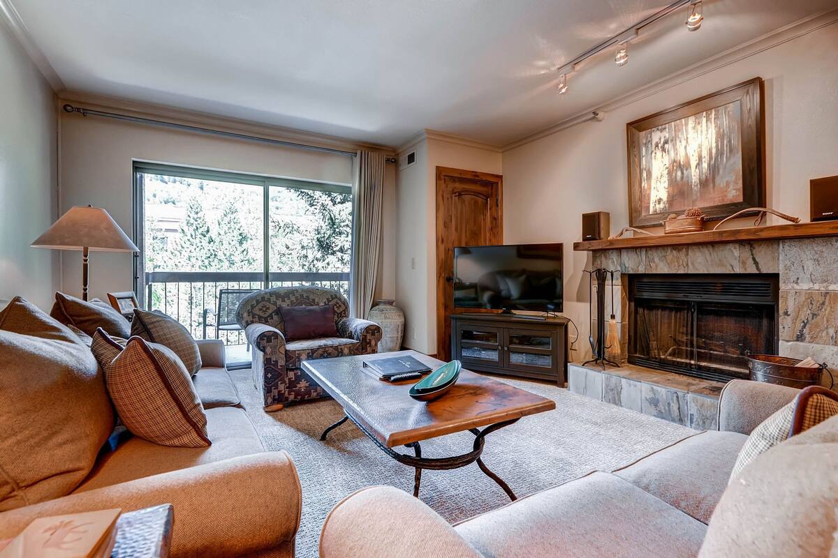 A living room with a sofa, armchair, and a coffee table. There is a fireplace with a TV above it.