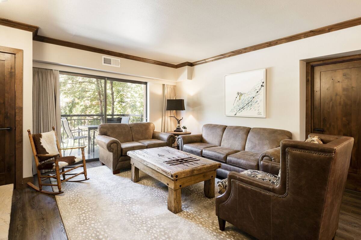 A living room with a large window, a wooden rocking chair, a brown leather sofa, and a coffee table.
