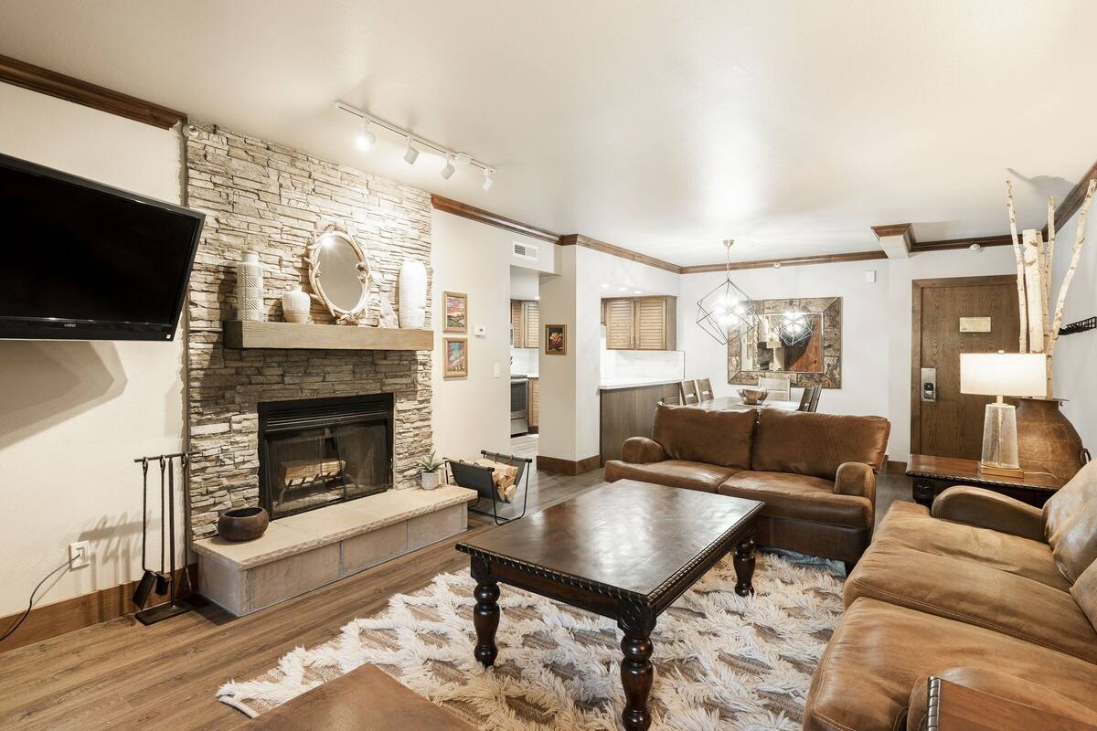 A living room with a stone fireplace, leather sofas, and a flat-screen TV.