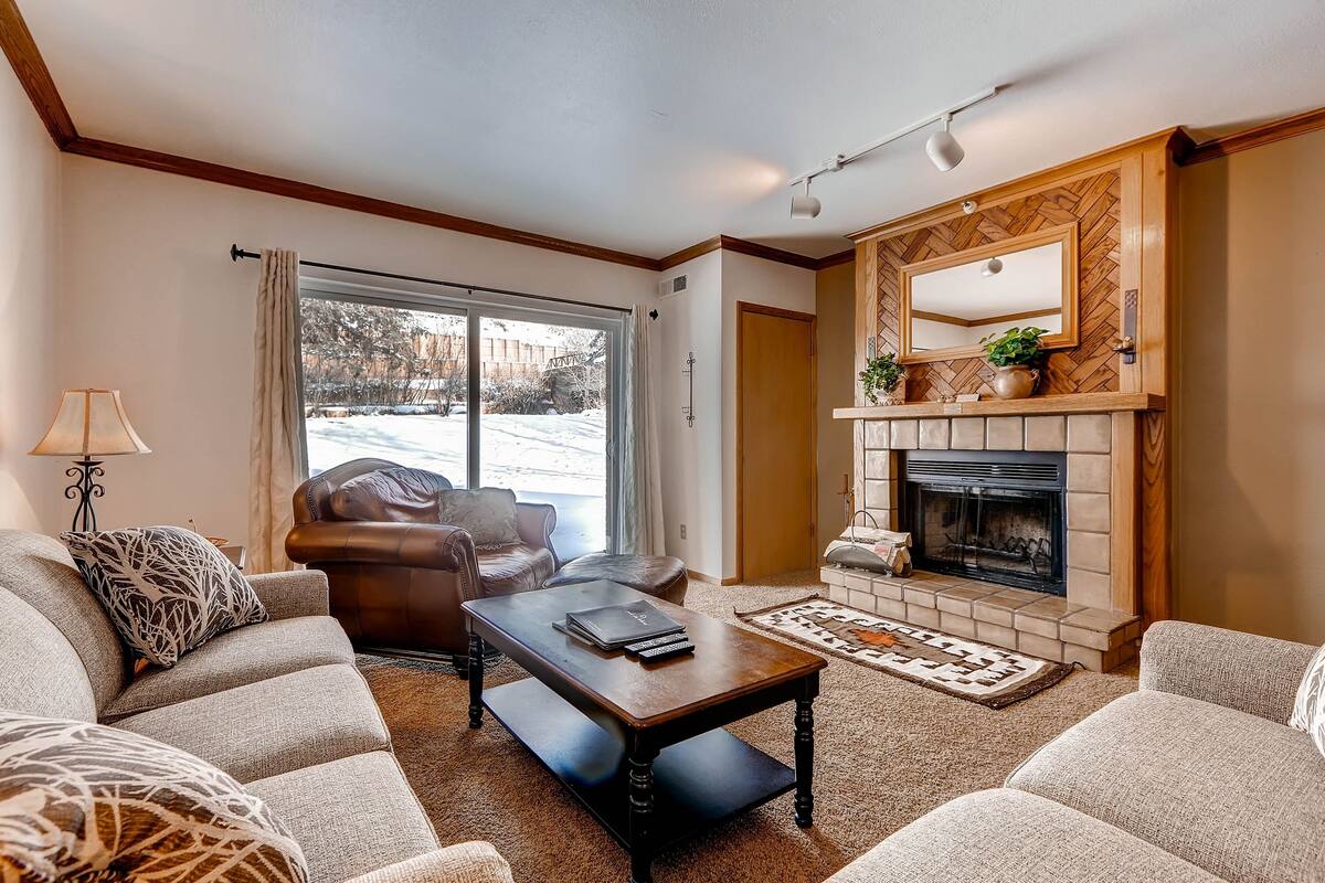 A living room with a fireplace, leather sofa, and a large window with a view of a snowy yard.