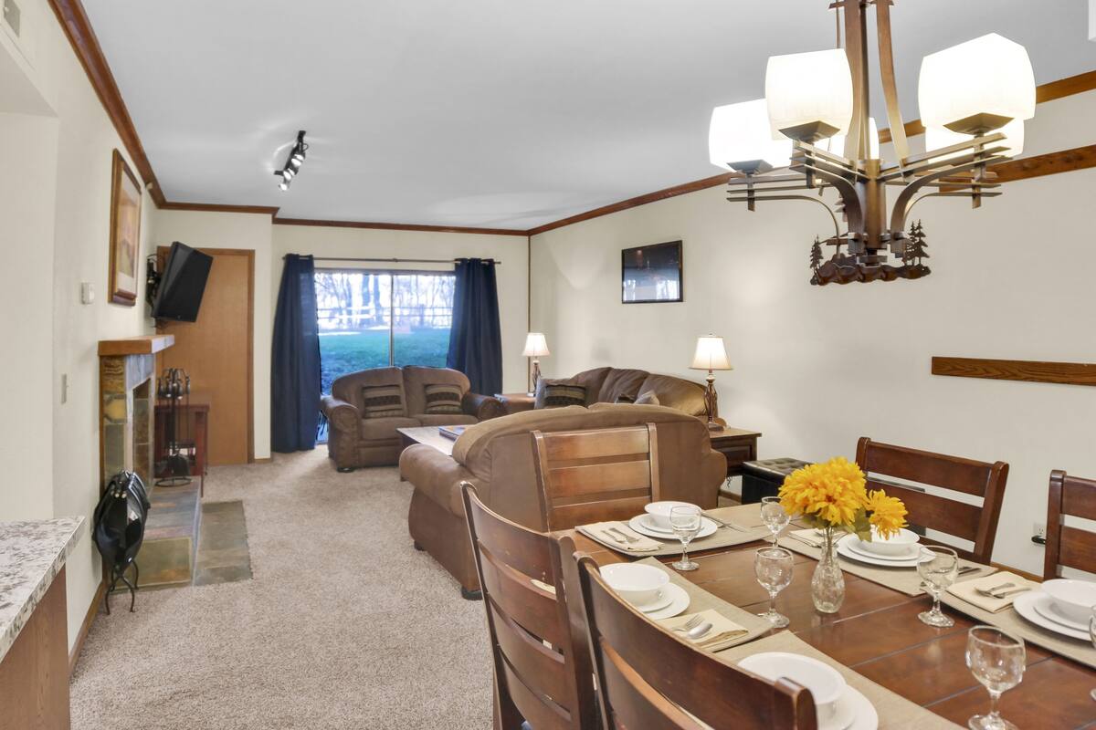 A dining area with a table set for four, a chandelier, and a view through a window.