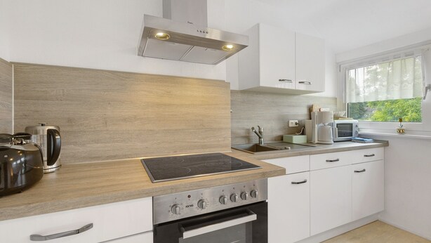 A modern kitchen with a built-in oven, a stovetop, and a window with a view of greenery. - Apartment 'Ruhepol, 75qm' with Shared Pool, Shared Garden and Wi-Fi (Vellmar)