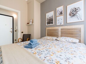 Un dormitorio ordenado con cama, mesita de noche, silla y puerta.