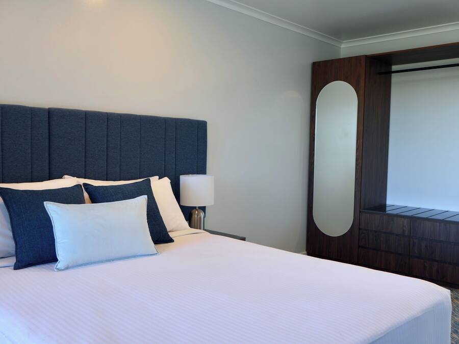 A hotel room with a large bed, a headboard, a nightstand, and a mirror.