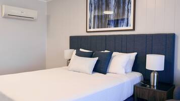 Habitación de hotel con cama, lámparas de noche, mesita de noche y un cuadro en la pared.
