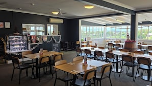A restaurant with tables and chairs, a dessert display, and large windows with a view. - Victory Hotel Motel Gympie  (Gympie)