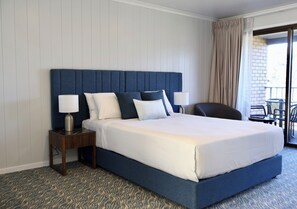 A hotel room with a large bed, two bedside tables with lamps, a view of the outside balcony, and a patterned carpet. - Victory Hotel Motel Gympie  (Gympie)