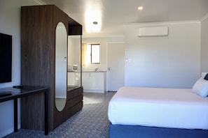 A bedroom with a bed, a dresser, a mirror, a TV, and a bathroom visible through an open door. - Victory Hotel Motel Gympie  (Gympie)