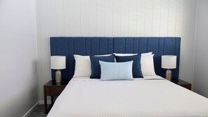 A hotel room with a large bed, white bedding, a blue headboard, two bedside lamps, and a patterned carpet. - Victory Hotel Motel Gympie  (Gympie)