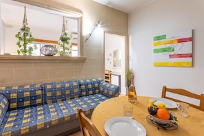 A dining area with a round table, a blue and yellow patterned sofa, and a wall with a colorful abstract painting.