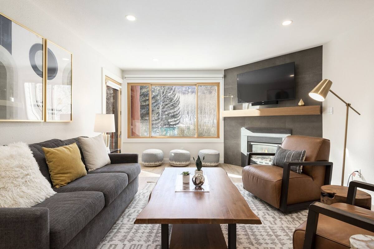 Ein modernes Wohnzimmer mit einem grauen Sofa, einem braunen Ledersessel, einem Holztisch und einem an der Wand montierten Fernseher.