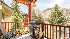 A balcony with a grill, chairs, and stacked firewood.