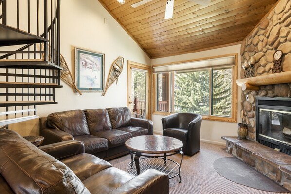 A cozy living room with a fireplace, leather sofas, a round coffee table, and a staircase with metal railings. - Park City Ski Resort UT - Snow Flower Condos (Park City)