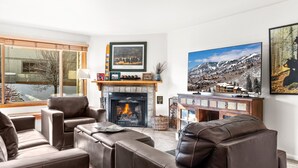 Een moderne woonkamer met leren banken, een open haard en grote ramen met uitzicht op een besneeuwde berg.
