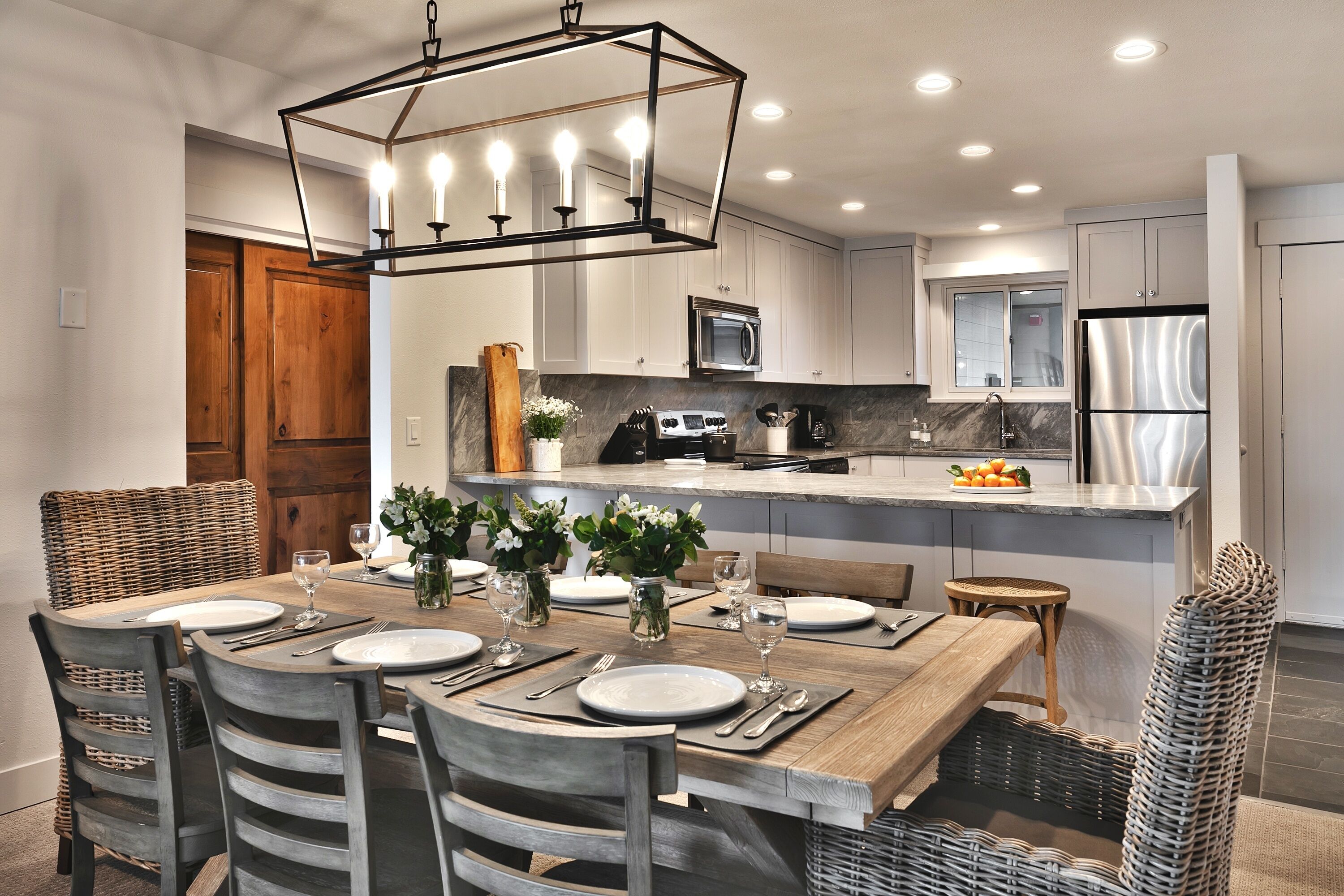 A modern kitchen with white cabinets, a stainless steel refrigerator, and a wooden dining table set for six.