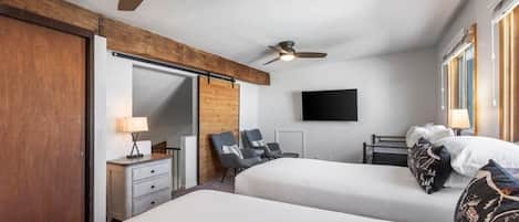 Habitación de hotel con dos camas, un escritorio, una silla, un televisor y un ventilador de techo.