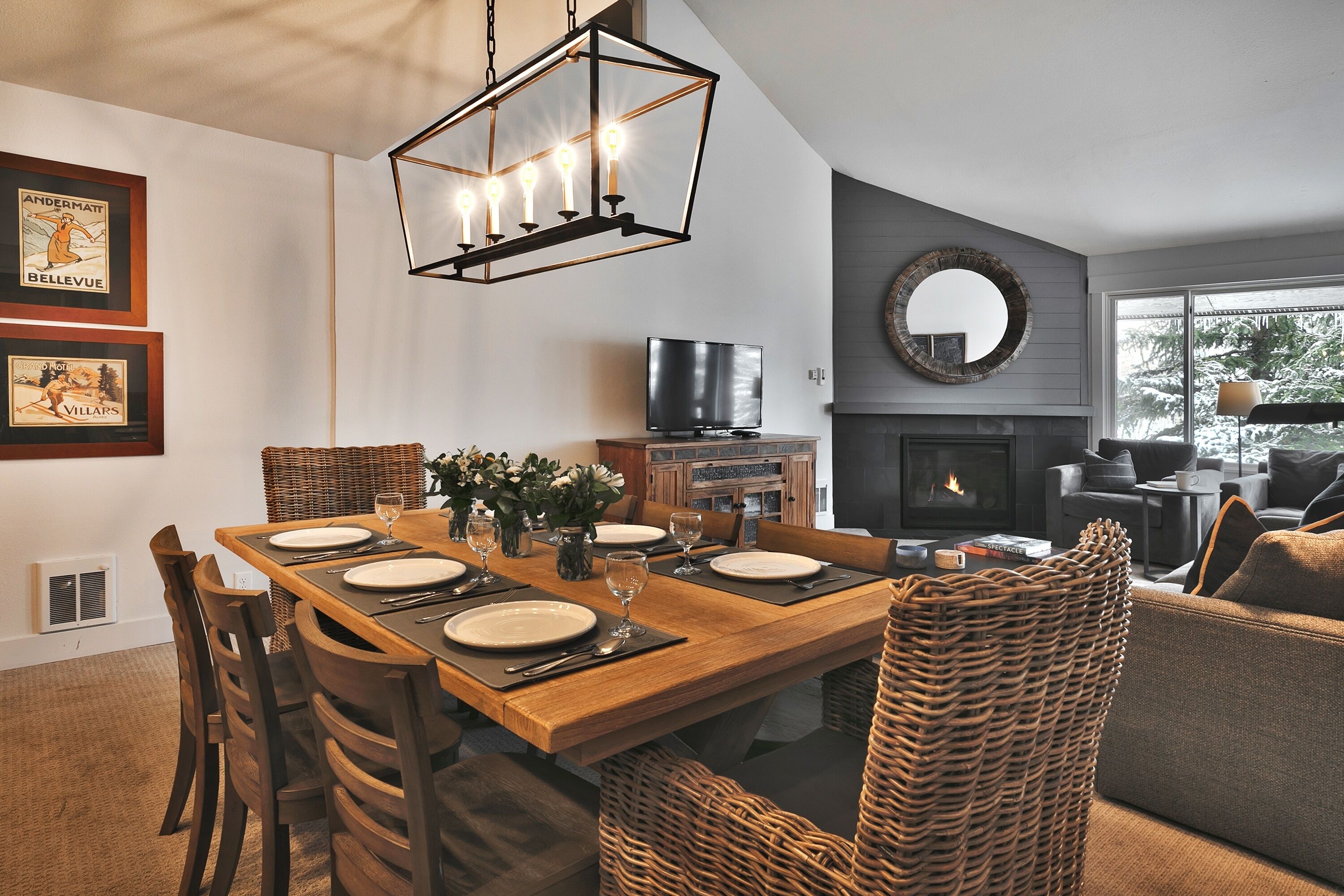A dining area with a wooden table set for four, a television, a fireplace, and wicker chairs.