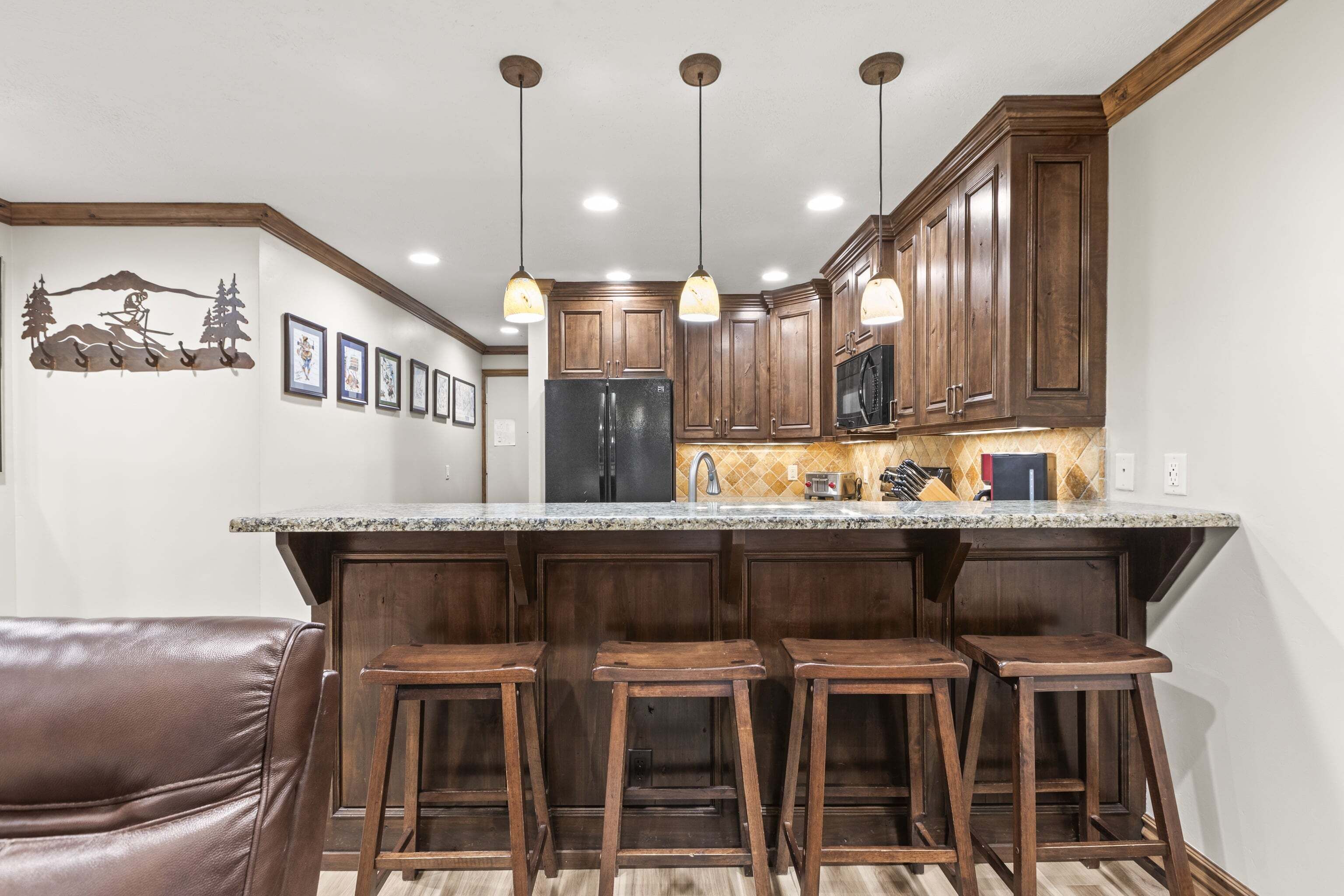 Una cocina con armarios de madera, encimera de granito y tres taburetes de bar.