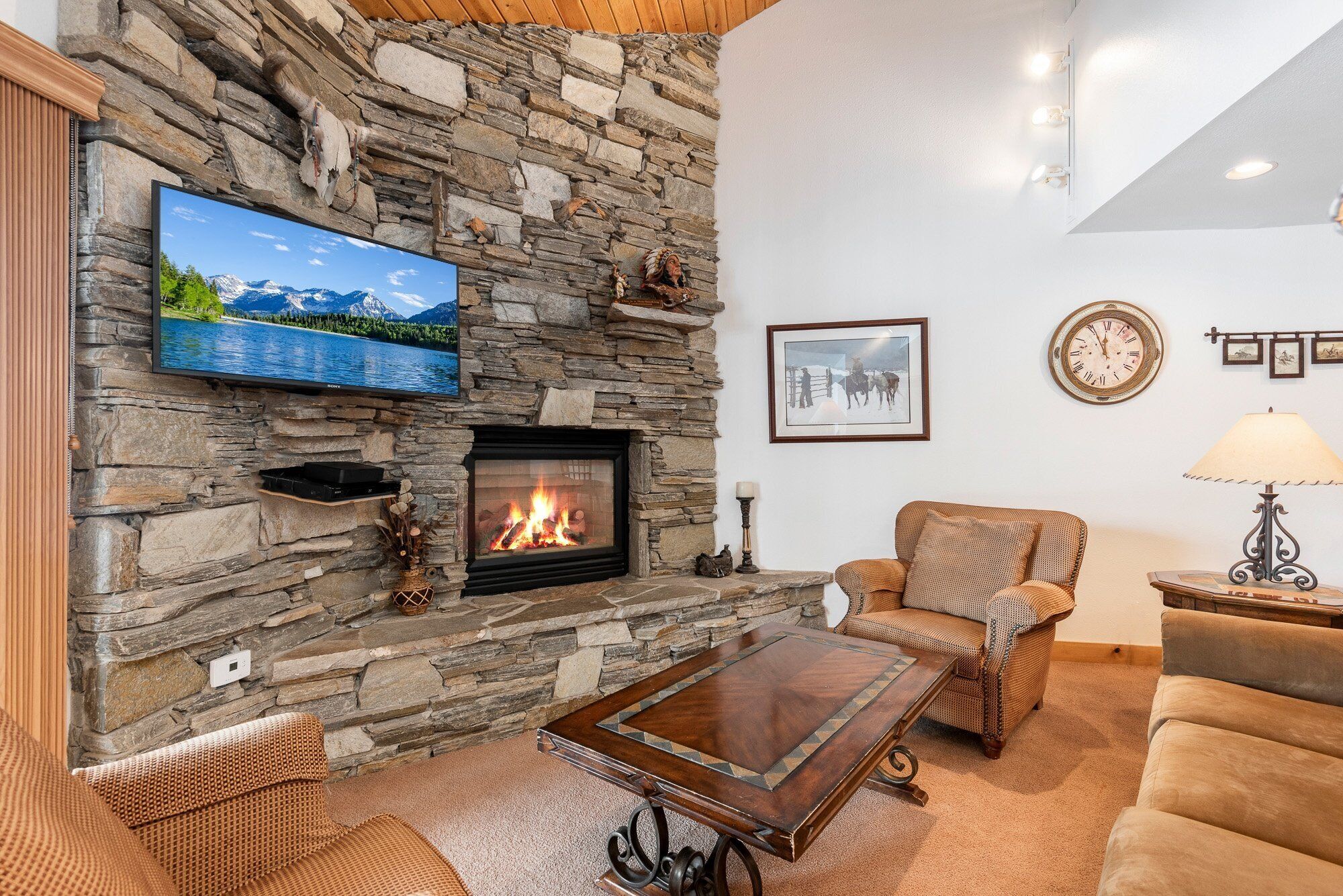 A cozy living room with a stone fireplace, a flat-screen TV, and comfortable seating.