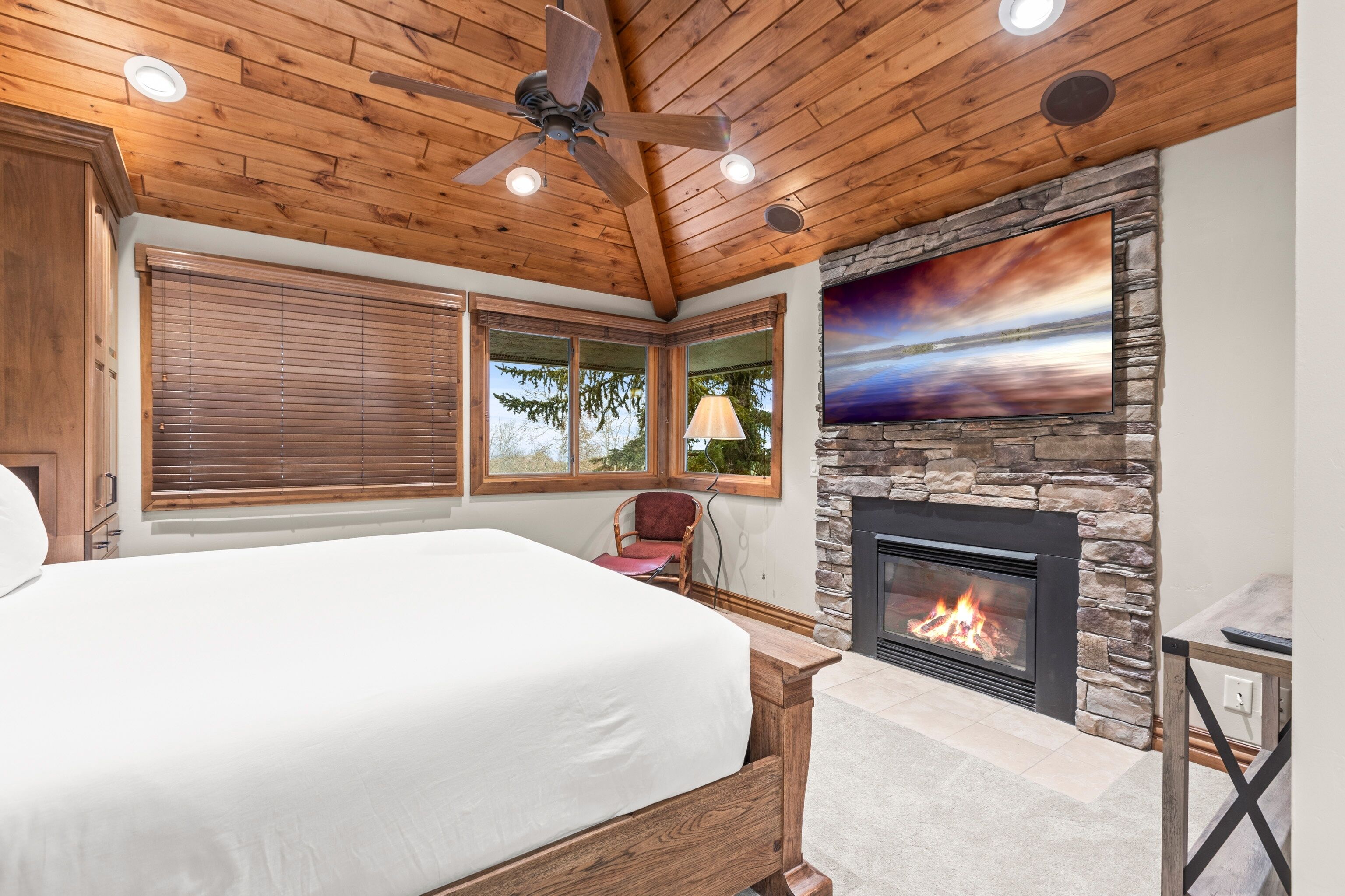 A bedroom with a large bed, a stone fireplace, and a ceiling fan.