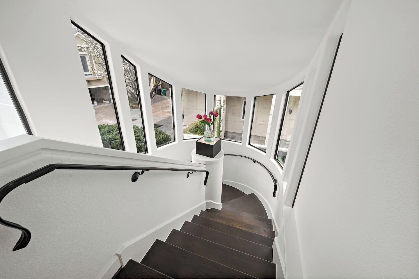 A curved staircase with dark wooden steps and white walls, leading to a landing with a vase of flowers.