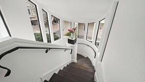Een gebogen trap met donkere houten treden en witte muren, leidend naar een plateau met een bloevas.