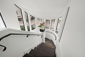 Een gebogen trap met donkere houten treden en witte muren, leidend naar een plateau met een bloevas.
