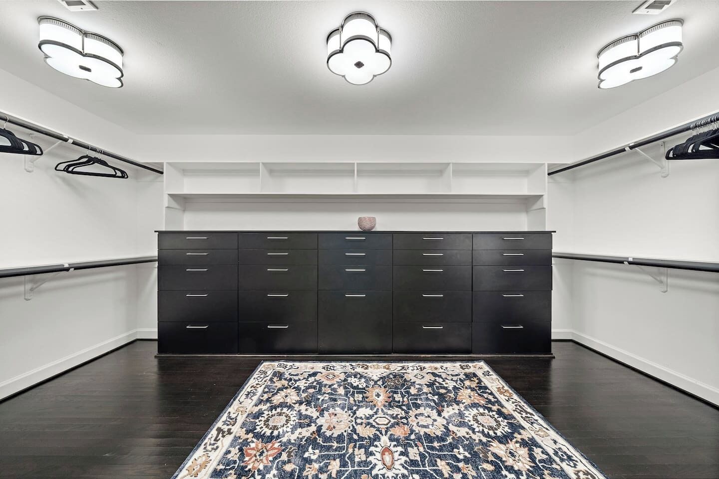 A walk-in closet with a large, patterned rug, a dark wooden wardrobe, and ceiling lights.