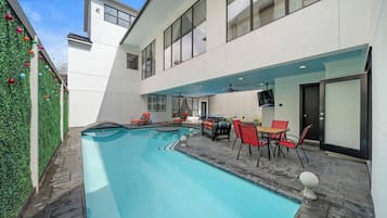 Un espace piscine extérieur moderne, doté de chaises longues et d’une table à manger.