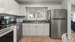Una cocina con armarios blancos, un refrigerador de acero inoxidable, un microondas y un lavamanos.