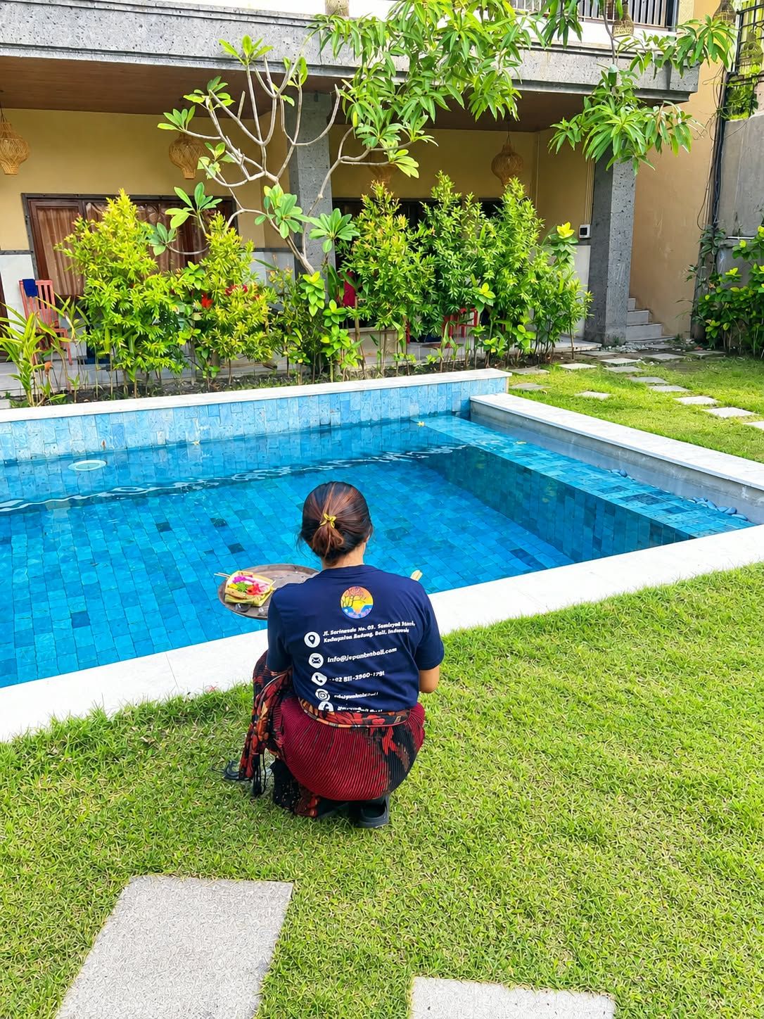 Eine Person sitzt an einem Schwimmbecken, im Hintergrund ein Gebäude.