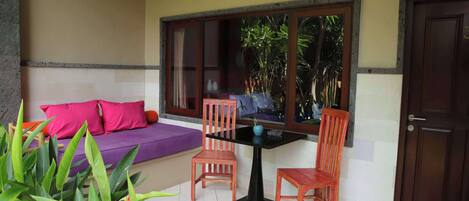 A room with a purple sofa, two wooden chairs, a small table, and a window with a view of greenery.