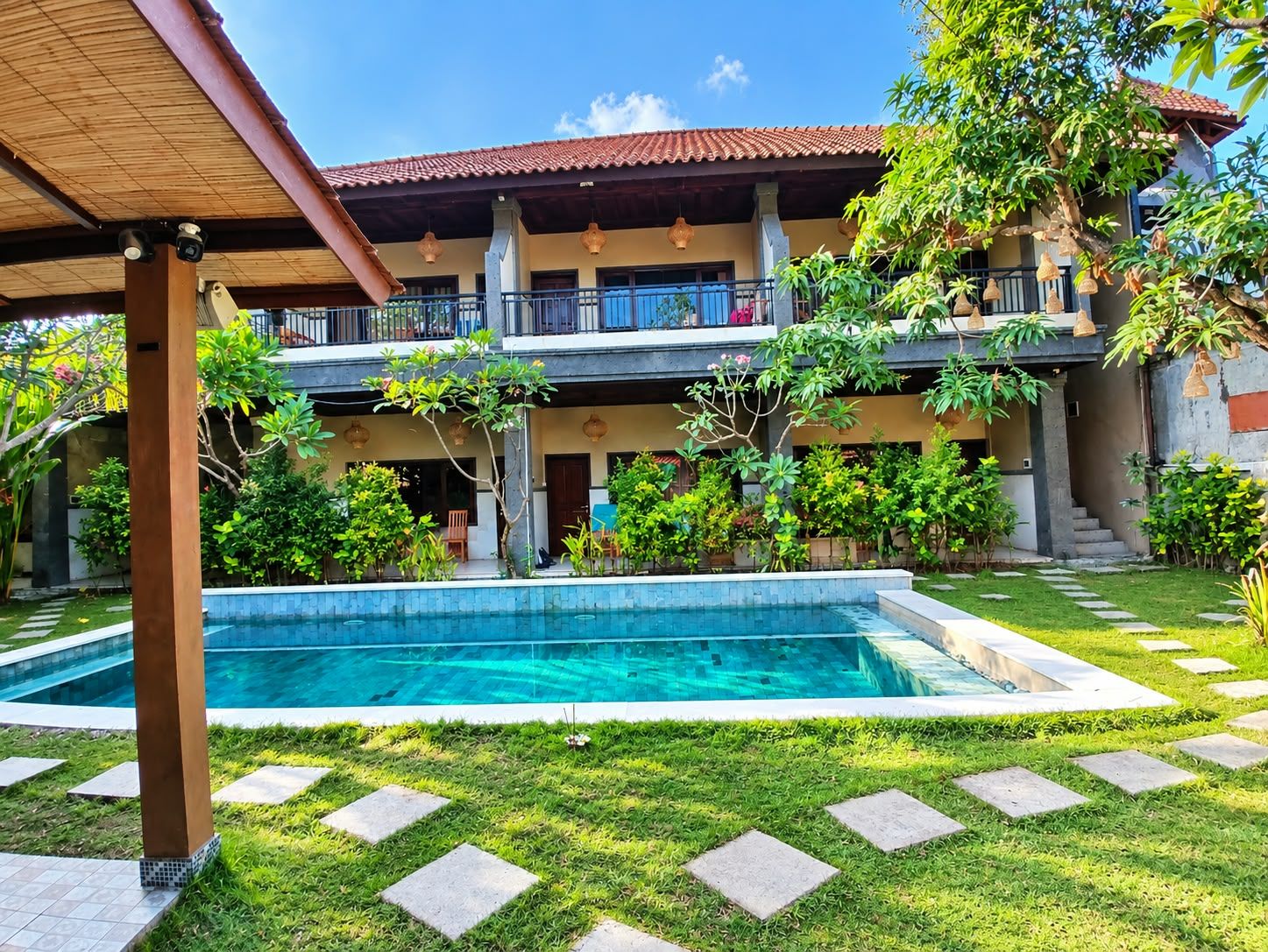 A two-story building with a swimming pool, surrounded by lush greenery and a covered patio area.