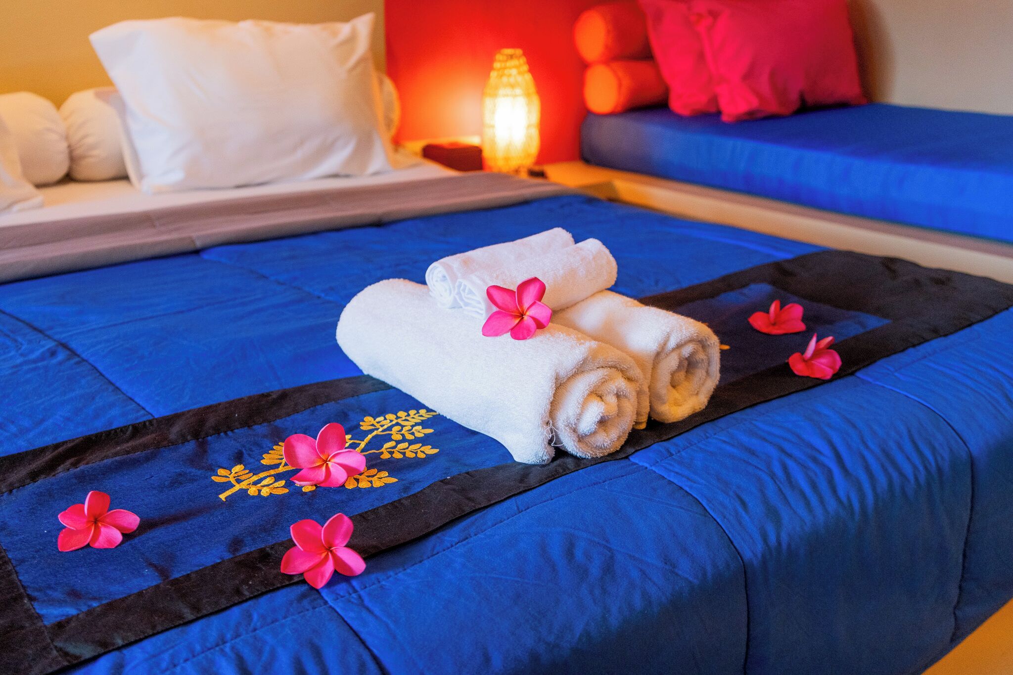 A neatly made bed with blue bedding, white towels, and pink flowers.