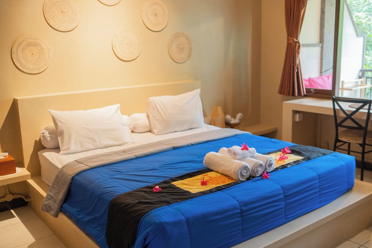 A neatly made bed with blue and black bedding, white pillows, and rolled towels with pink flowers.