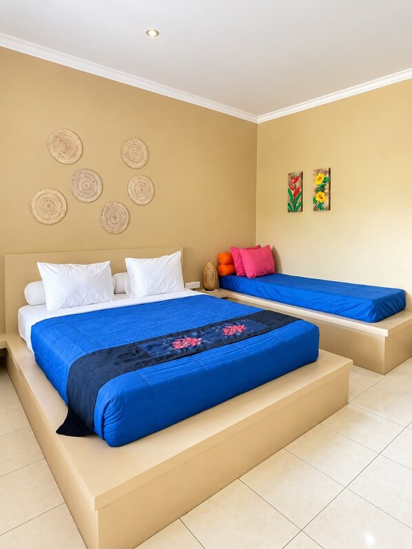 A hotel room with a large bed, a smaller bed, and a sofa bed. There are decorative wall art pieces and a small table with a vase.