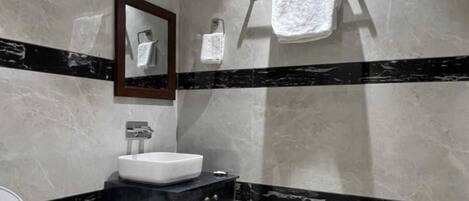 A bathroom with a white sink, dark cabinet, and a mirror above it. There are two towels hanging on the wall.