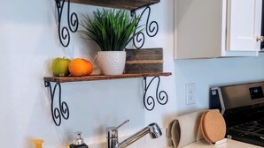 A kitchen with two stainless steel sinks, a wooden shelf with decorative items, and a potted plant.