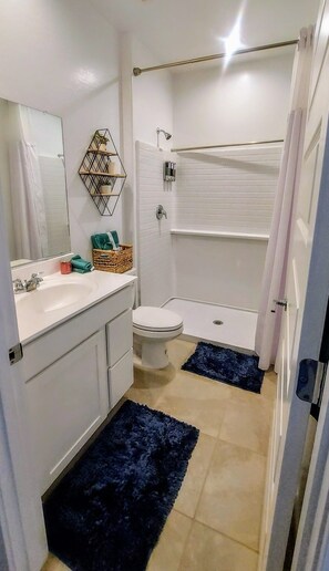 Un baño con lavamanos, inodoro y bañera blancos. Hay dos alfombras azules en el suelo.