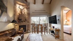 A cozy living room with a stone fireplace, a leather sofa, a wooden coffee table, and a TV mounted on the wall. - Park City Ski Resort UT - Snow Flower Vacation Homes (Park City)