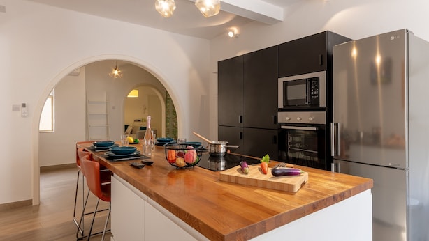 A modern kitchen with a wooden countertop, stainless steel appliances, and a central island with bar stools. - Magnificent Sea View Penthouse Cospicua (Cospicua)