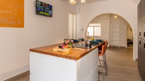 A modern kitchen with a wooden island, white cabinetry, and a TV mounted on the wall. - Magnificent Sea View Penthouse Cospicua (Cospicua)