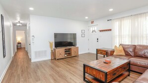 Un salon moderne avec un parquet, un canapé en cuir, une table basse en bois et un téléviseur posé sur un meuble en bois.