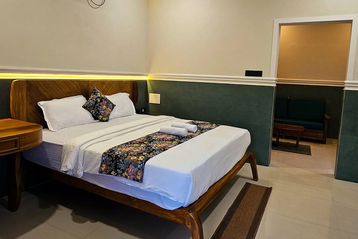 A hotel room with a bed, bedside tables, a green sofa, a ceiling fan, and an air conditioning unit.