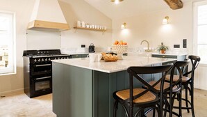 A kitchen with a large island, dark wooden chairs, and a built-in oven. - Pressoir de la Fleur (néac)