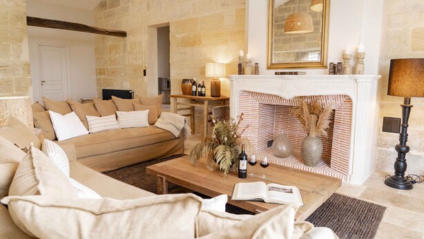 A cozy living room with a fireplace, a sofa, a coffee table with books and bottles, and a lamp. - Pressoir de la Fleur (néac)