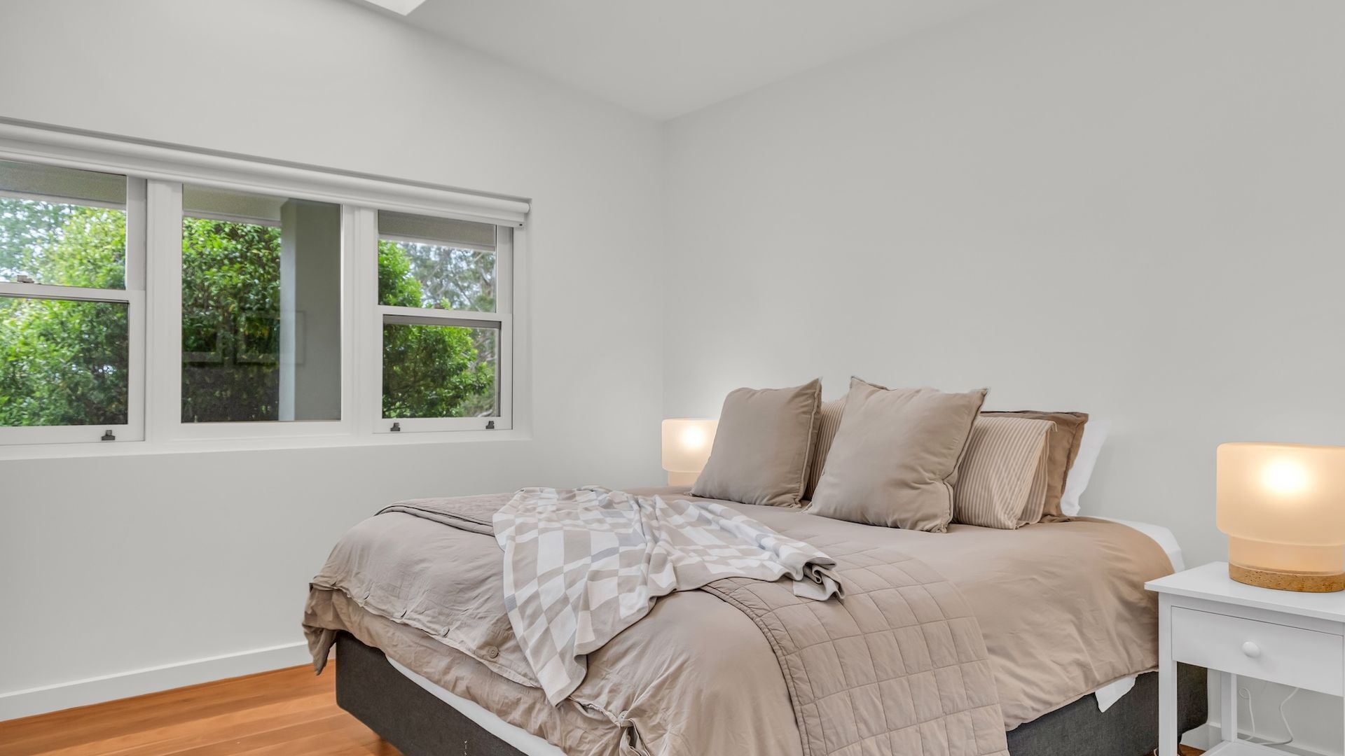 A bedroom with a bed, a nightstand, and a window with a view of trees.