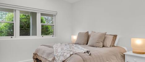 A bedroom with a bed, a nightstand, and a window with a view of trees.